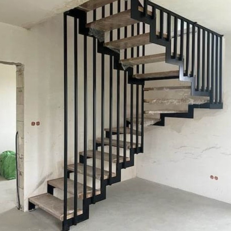 Nowoczesne schody spiralne z czarną metalową konstrukcją i drewnianymi stopniami w surowym stanie, z widocznymi elementami montażowymi i niedokończonymi ścianami.