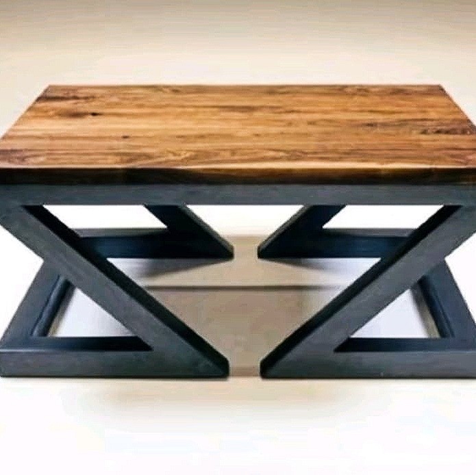 Kwadratowy stolik kawowy z blatem z drewna o ciepłym odcieniu i podstawą z ciemnego metalu w kształcie litery X, widoczny w neutralnym wnętrzu.