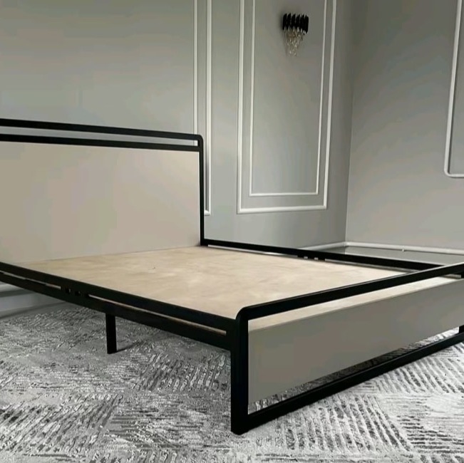 Metalowa rama łóżka z tapicerowanymi panelami w minimalistycznym wnętrzu z szarą ścianą i dekoracyjną listwą.