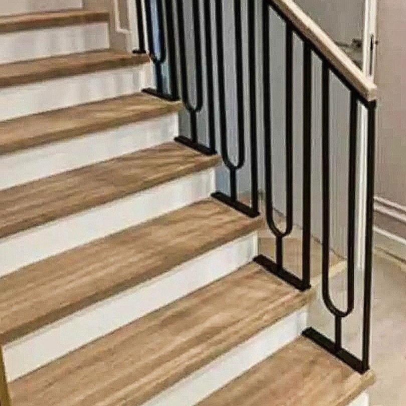 Schody z drewnianymi stopniami i czarną, metalową balustradą o nowoczesnym designie, z elementami dekoracyjnymi w kształcie litery U, zakończoną drewnianą poręczą.