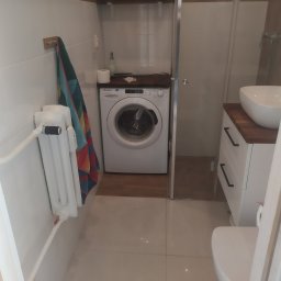 Ryszard Kowalewski - Wnętrze łazienki z pralką Candy umieszczoną pod blatem, białą umywalką nablatową na szafce z ciemnym blatem i białym grzejnikiem żeberkowym z kolorowym ręcznikiem.