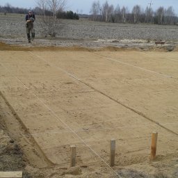 ZDAN -BUDOWNICTWO Sp. z o.o. - Przygotowany teren pod fundamenty domu z wytyczonymi liniami i wbitymi słupkami, widoczni pracownicy w tle.