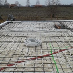 ZDAN -BUDOWNICTWO Sp. z o.o. - Przygotowanie płyty fundamentowej z instalacją ogrzewania podłogowego, widoczne zbrojenie, rury grzewcze w kolorze białym i czerwonym, oraz izolacja obwodowa z białego styropianu.