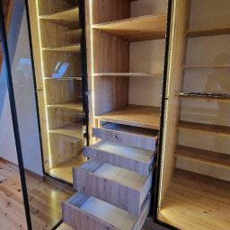 NOWY WYMIAR MEBLI AGATA PIECHOTA - Wnętrze drewnianej szafy z oświetleniem LED, z trzema wysuniętymi szufladami i półkami, widoczne okucia szuflad.