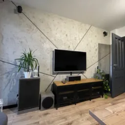 Szara ściana z efektem betonu i geometrycznymi czarnymi liniami, telewizor, drewniana podłoga i meble w salonie.