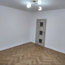 M&M Remonty - Pomalowane na biało ściany i ułożona parkietowa podłoga w pokoju z zamontowanymi drzwiami wewnętrznymi i nowoczesną lampą sufitową.