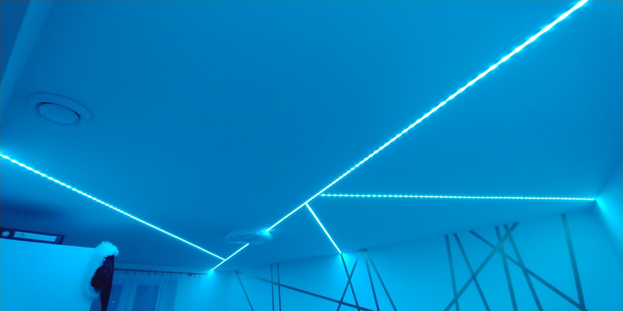 Pokój oświetlony niebieskimi listwami LED na suficie i ścianach, tworzącymi geometryczny wzór.