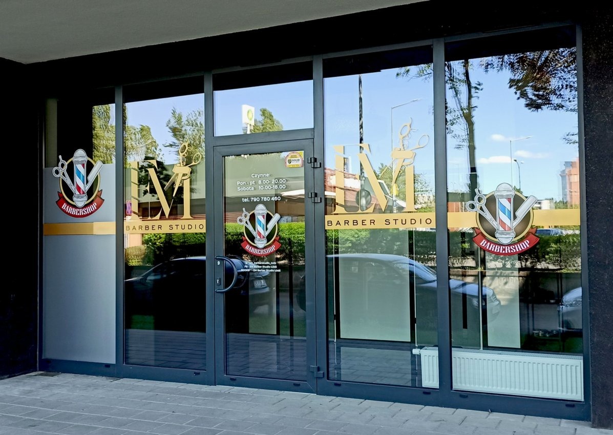 Szklana fasada salonu fryzjerskiego z naklejonym logo i informacjami o godzinach otwarcia, widoczne odbicia samochodów i otoczenia.