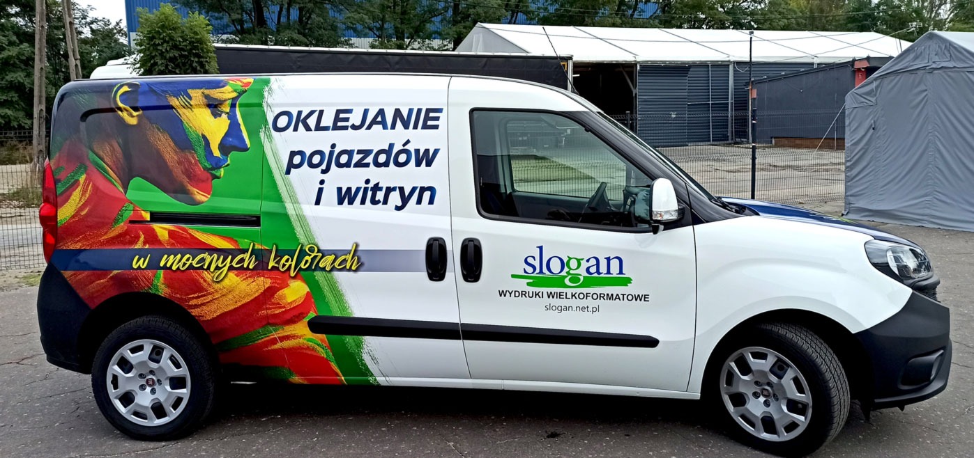 Biały samochód dostawczy z kolorową grafiką przedstawiającą profil twarzy i napisem 'Oklejanie pojazdów i witryn w mocnych kolorach' oraz logo firmy z hasłem 'wydruki wielkoformatowe'.