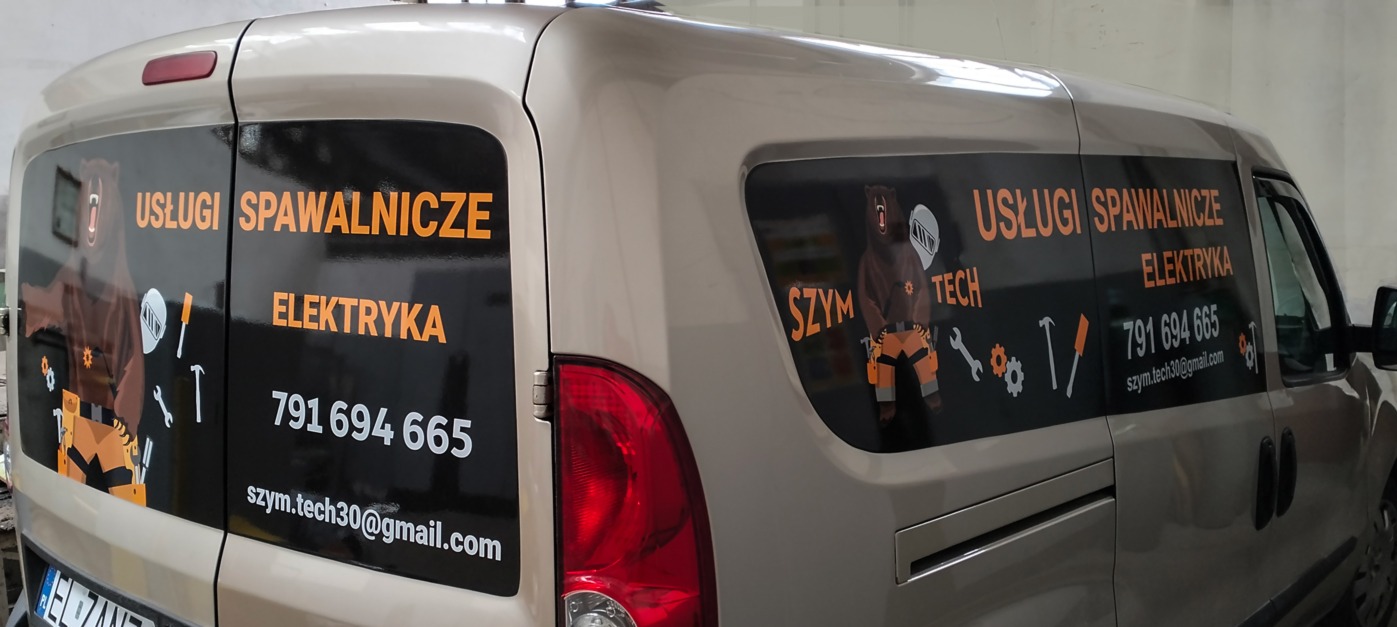 Oklejony samochód firmy Szym Tech oferującej usługi spawalnicze i elektryczne, z grafiką niedźwiedzia w kombinezonie i narzędziami.