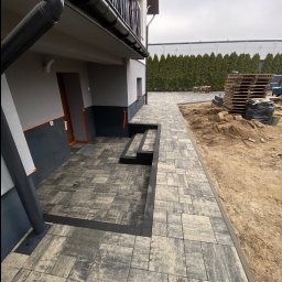 Volodymyr Yarmyshko - Ułożona kostka brukowa w Warszawie, tworząca ścieżkę i schody przed domem. Widoczne palety z kostką i przygotowany teren pod dalsze prace.