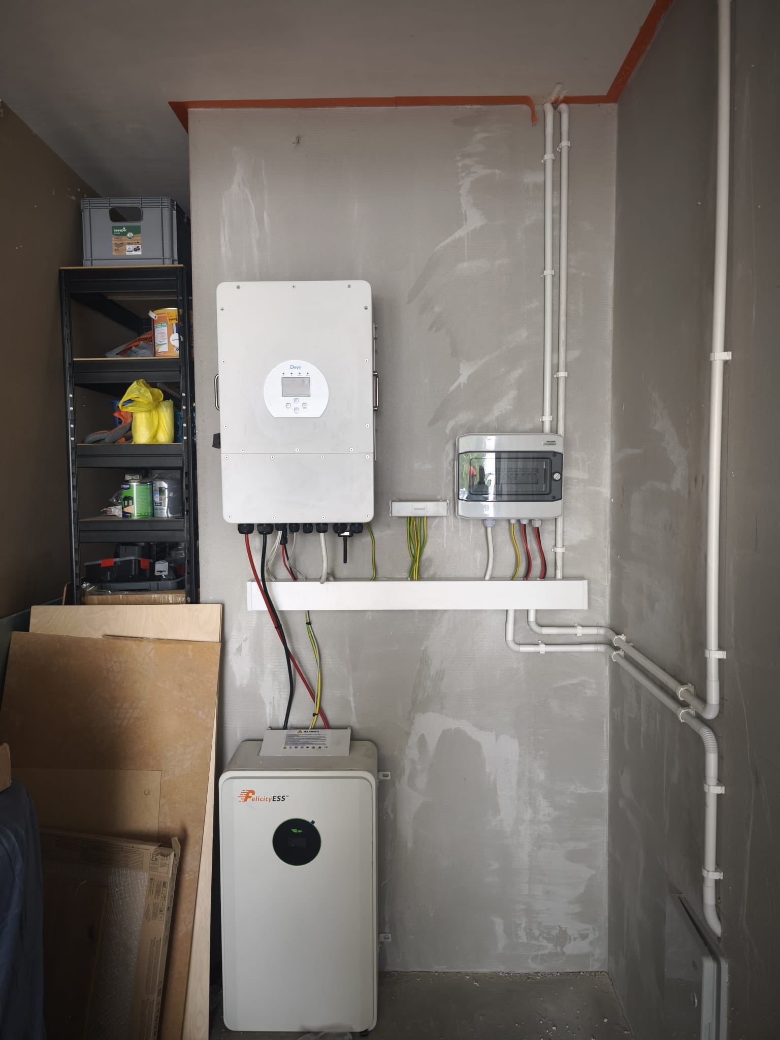 Wnętrze z zamontowanym falownikiem hybrydowym Deye i magazynem energii FelicityESS. Widoczne okablowanie i instalacja elektryczna na surowej ścianie.