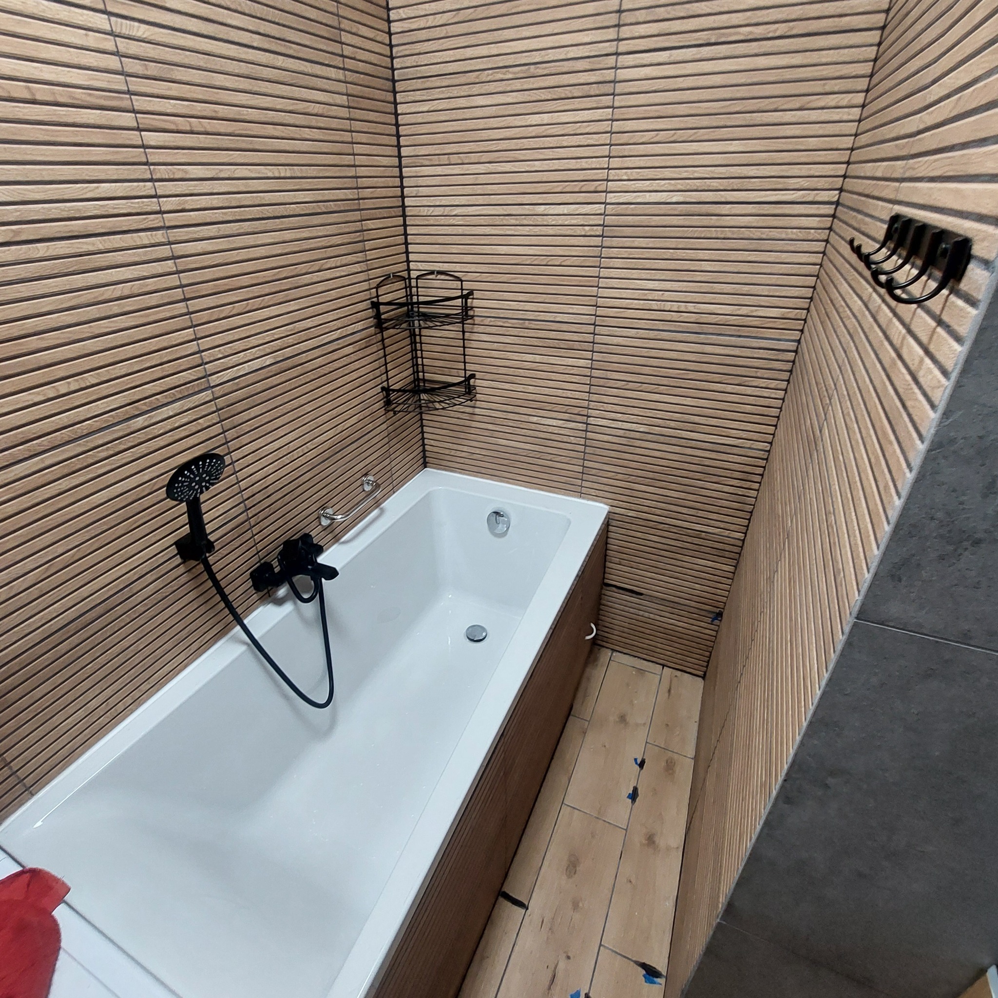 Nowoczesna łazienka po remoncie w Szamocinie z wanną, drewnopodobnymi płytkami na ścianach ułożonymi poziomo i czarną armaturą.