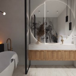 Pod Klucz Agata Malinowska - Nowoczesna łazienka z okrągłym lustrem podświetlanym LED, marmurowym blatem i drewnianymi szafkami, złota armatura, dekoracyjny bukiet w wazonie, widoczna wanna.