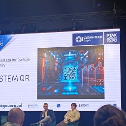 Tetiana Ivankova Global Clean Kraków - Prezentacja na targach Clean-Tech Expo z systemem QR dla branży czystości, logo PIGC i Ptak Warsaw Expo widoczne na ekranie. Prelegenci siedzą na krzesłach.
