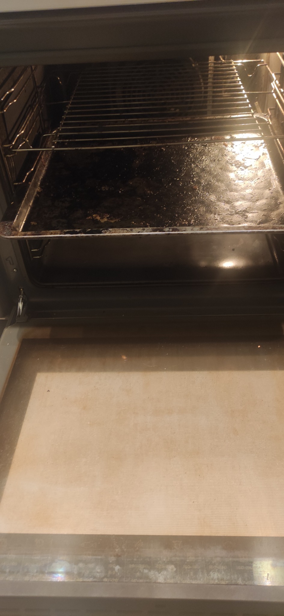 Wnętrze brudnego piekarnika z przypalonymi resztkami jedzenia na blasze i ruszcie.