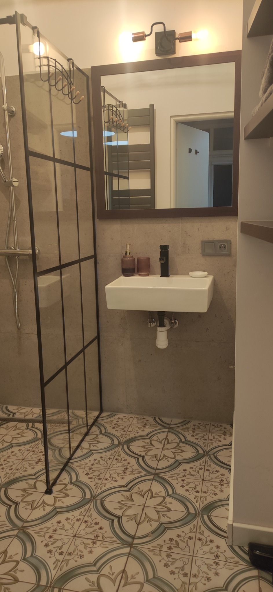 Nowoczesna łazienka z kabiną prysznicową typu walk-in, umywalką nablatową z czarną armaturą i dekoracyjną podłogą w kwiatowe wzory.