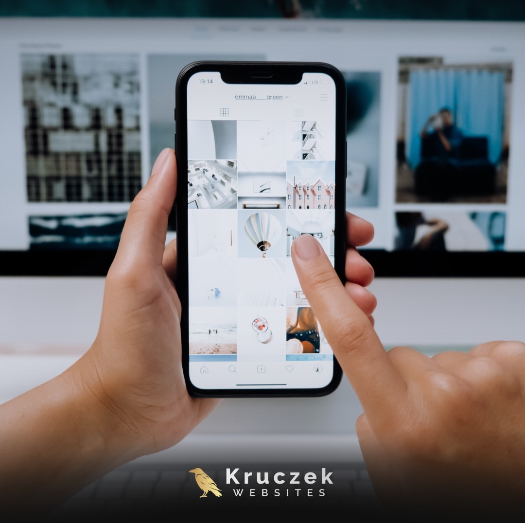 Osoba przegląda portfolio na telefonie komórkowym, w tle widoczny ekran komputera z otwartą stroną internetową. Na dole logo firmy Konrad Kruczek Websites.
