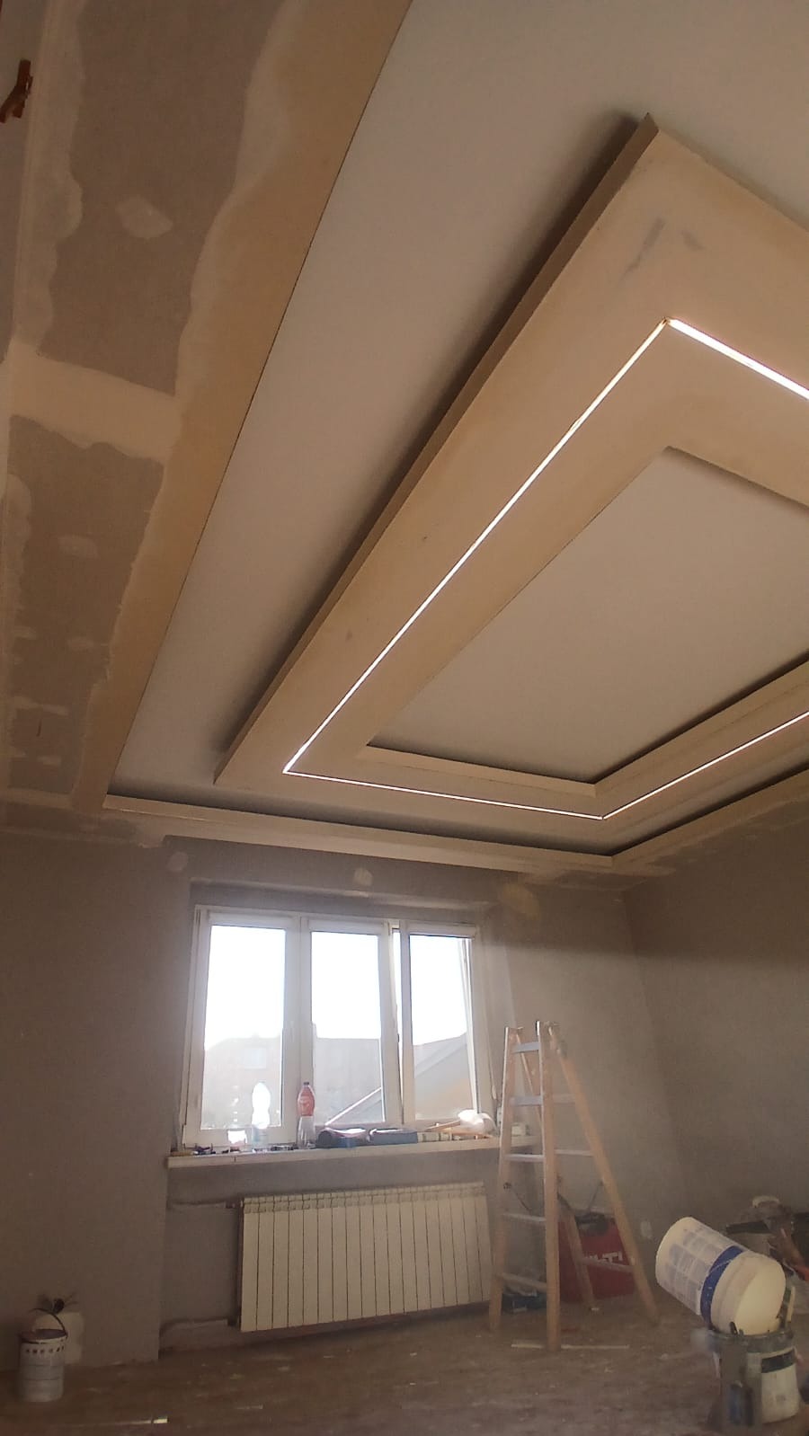 Wykończony sufit podwieszany z oświetleniem LED w kształcie kwadratu, widoczny w remontowanym pomieszczeniu z drabiną i narzędziami.