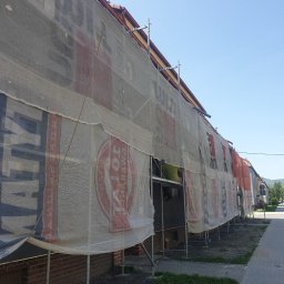 DAMIAN BUD - Budynek w trakcie remontu elewacji, osłonięty siatką z reklamami, widoczne rusztowania i fragment pracującego robotnika.