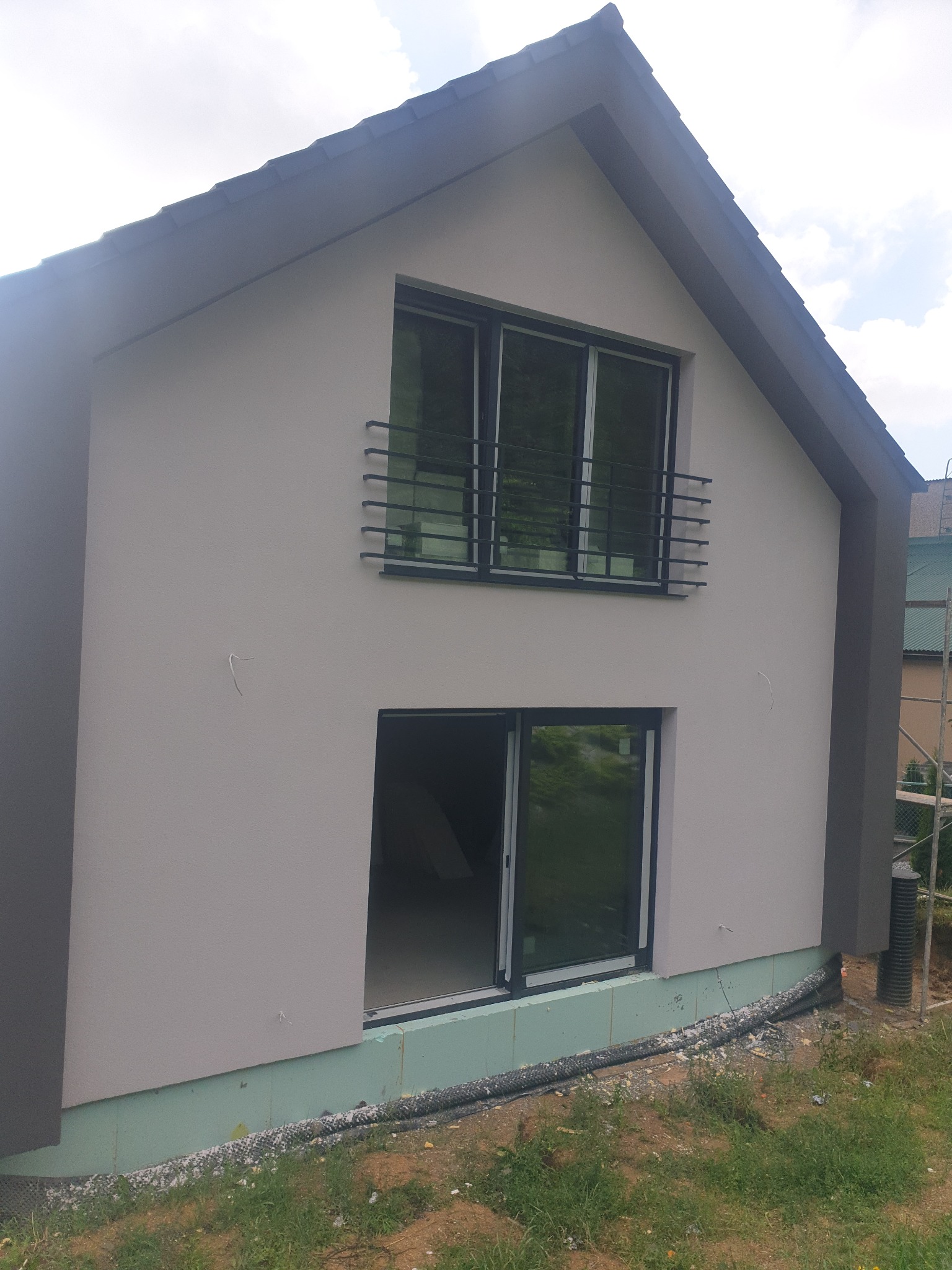 Nowoczesny dom jednorodzinny w trakcie wykańczania elewacji, widoczne ocieplenie fundamentów i świeżo otynkowana ściana z zamontowanymi oknami