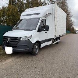 FIRMA HANDLOWO-USŁUGOWA Daniel Wencki - Biały Mercedes-Benz Sprinter z plandeką, zaparkowany na poboczu drogi, widok z boku na tle drzew i pochmurnego nieba.