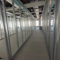 USŁUGI OGÓLNOBUDOWLANE Tomasz Radtke - Metalowa konstrukcja szkieletowa ścian działowych w surowym stanie, widoczne profile pionowe i poziome, instalacje pod sufitem, przygotowanie do dalszych prac wykończeniowych w nowym budynku.
