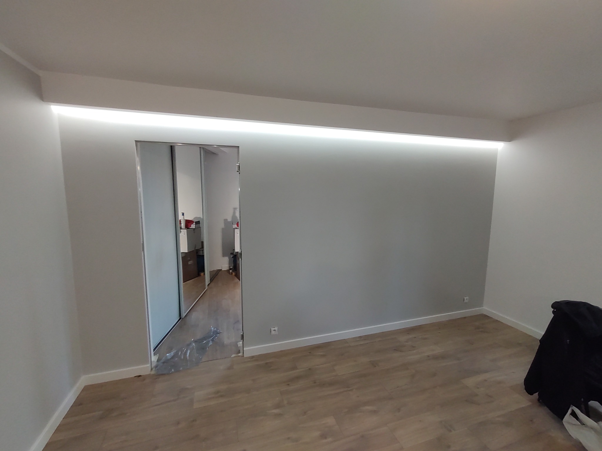 Nowoczesne wnętrze z przesuwnymi szklanymi drzwiami, podświetlanym sufitem i panelami podłogowymi, widok z perspektywy pokoju z widocznym workiem na podłodze.