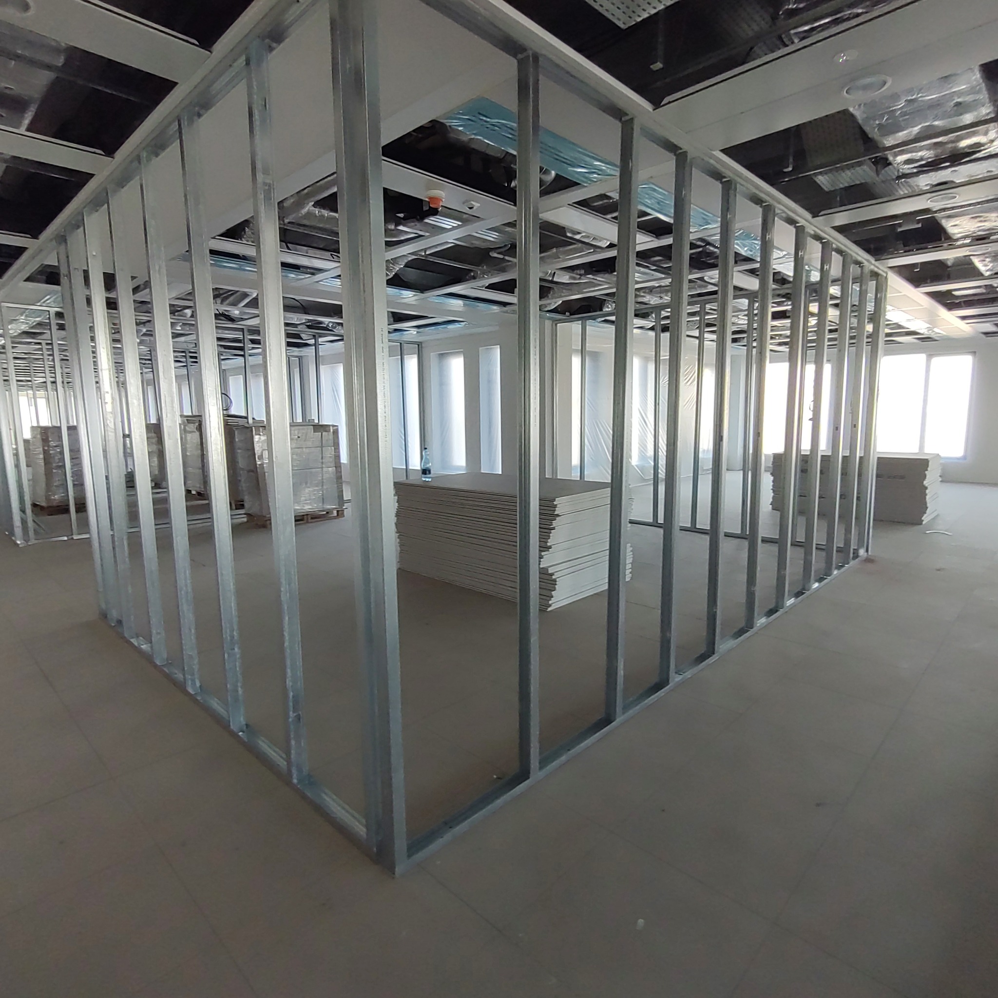 Stelaż z profili stalowych tworzący ścianę działową w surowym stanie, widoczne płyty gipsowo-kartonowe i instalacje pod sufitem.