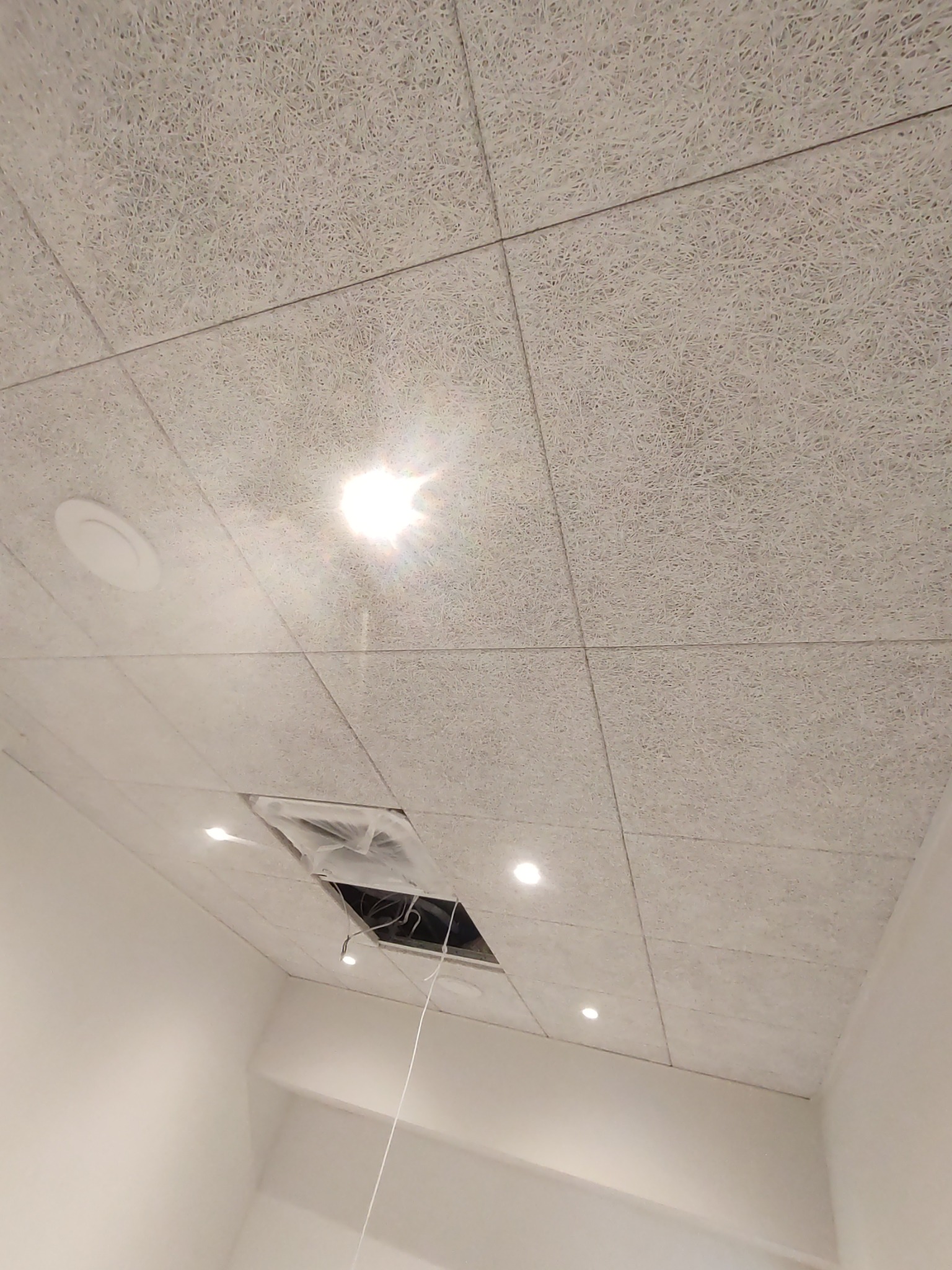 Panelowy sufit z fakturą włókien, z widocznymi punktowymi lampami LED, kratką wentylacyjną i otwartym otworem z przewodami.