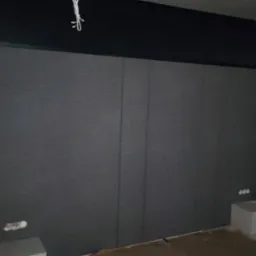 Szara ściana z paneli ściennych z widocznymi listwami dekoracyjnymi, fragment instalacji elektrycznej i niedomalowane fragmenty ściany.