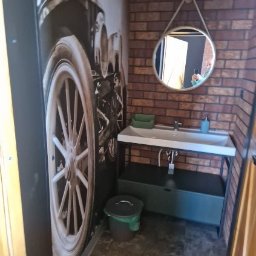 GLAZURNIK PL USŁUGI OGÓLNOBUDOWLANE DAMIAN WIERZBICKI - Łazienka w stylu retro z tapetą z motywem koła samochodu, ceglaną ścianą i okrągłym lustrem na sznurku. Umywalka na metalowym stelażu, kosz na śmieci.