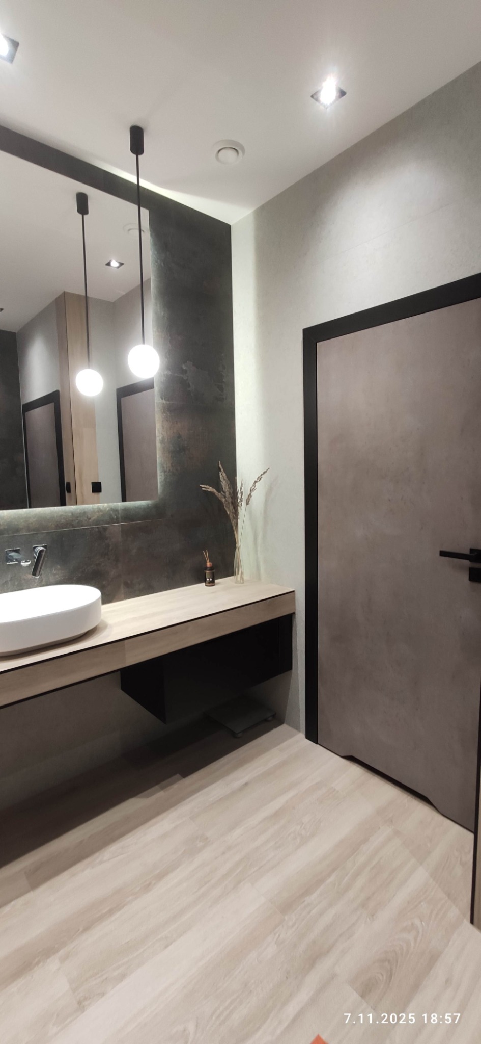 Nowoczesna łazienka z drewnopodobną podłogą, umywalką nablatową i lustrem z okrągłymi lampami. Minimalistyczny design z akcentami dekoracyjnymi.