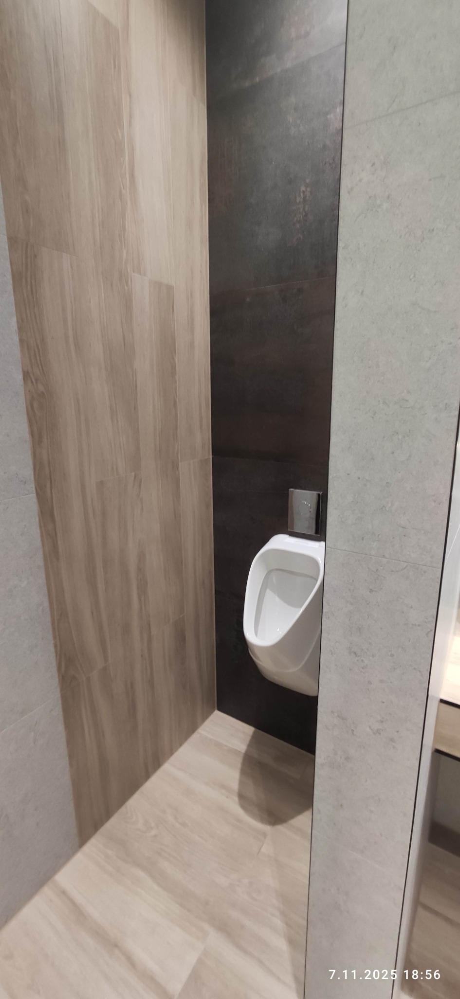 Nowoczesna toaleta z pisuarami w Nowym Tomyślu. Ściany wyłożone płytkami w odcieniach szarości i brązu. Minimalistyczny design, czyste linie i neutralna kolorystyka.