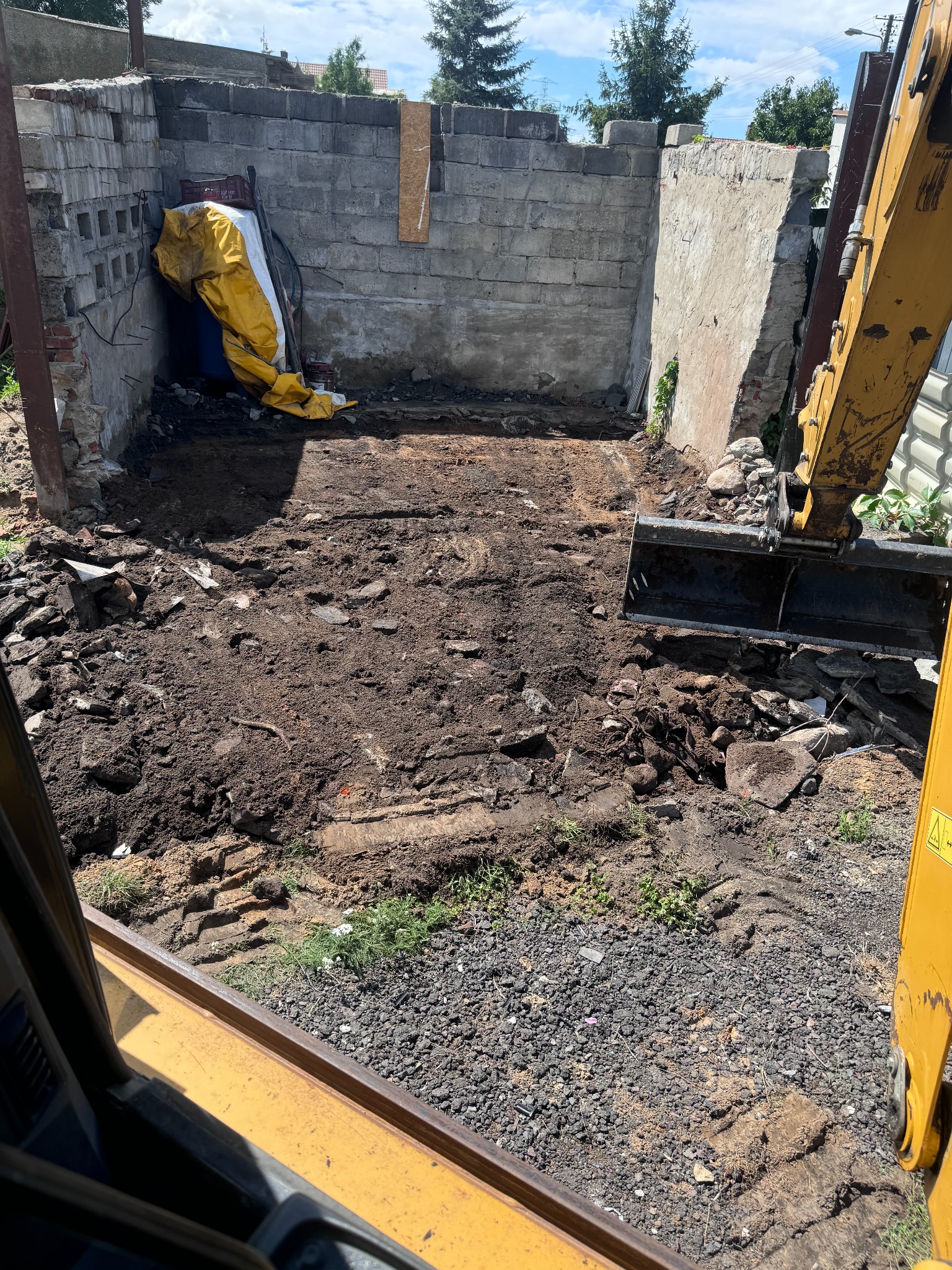 Żółta koparka na placu budowy po rozbiórce, z gruzem i ziemią, widok z wnętrza kabiny.