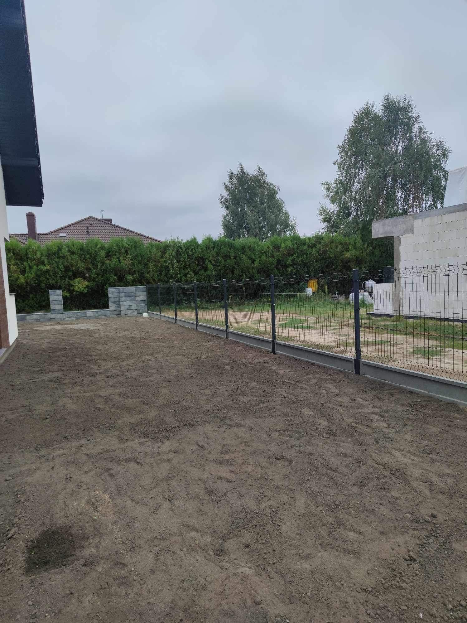 Nowo postawione, panelowe ogrodzenie z podmurówką betonową na wyrównanym, przygotowanym podłożu, widok na ogród i fragment domu w tle.