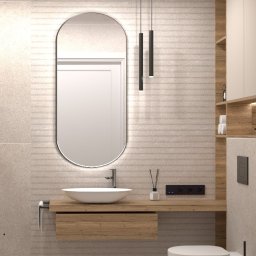 Julija Leszczanok - Nowoczesna łazienka w beżowej kolorystyce z umywalką nablatową, owalnym lustrem z podświetleniem LED, wiszącą toaletą i drewnopodobną szafką pod umywalką oraz półkami.