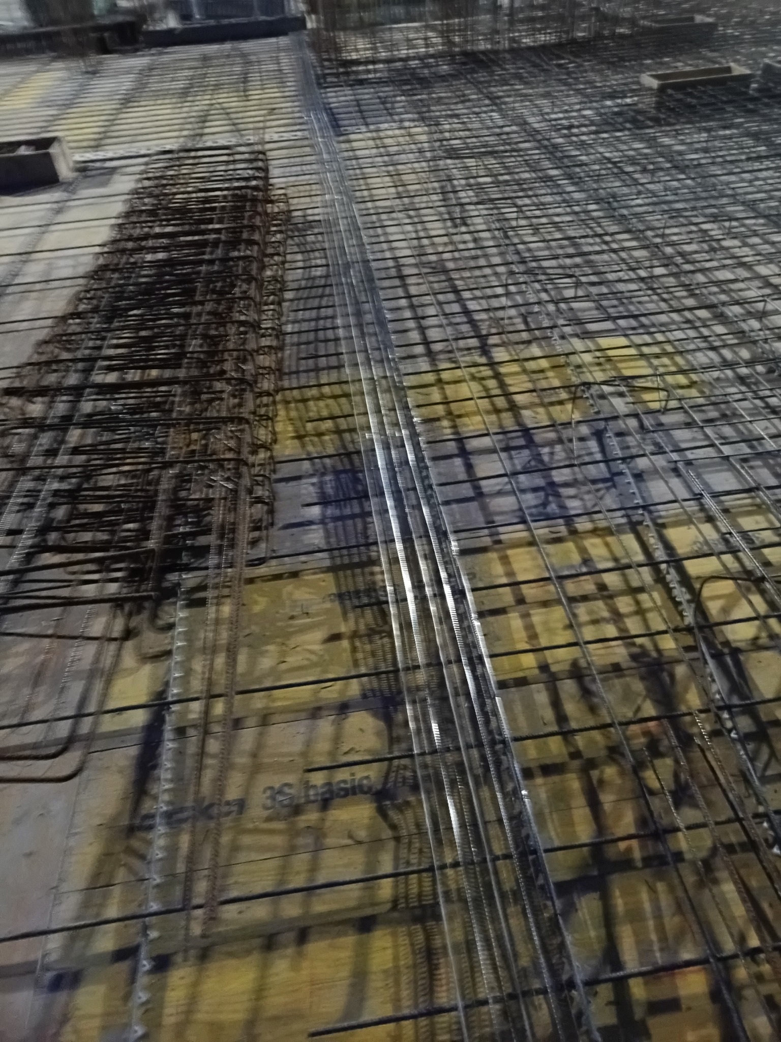 Zbrojenie fundamentów ułożone na deskowaniu, widoczne stalowe pręty i siatki zbrojeniowe przygotowane do zalania betonem, widok z góry.