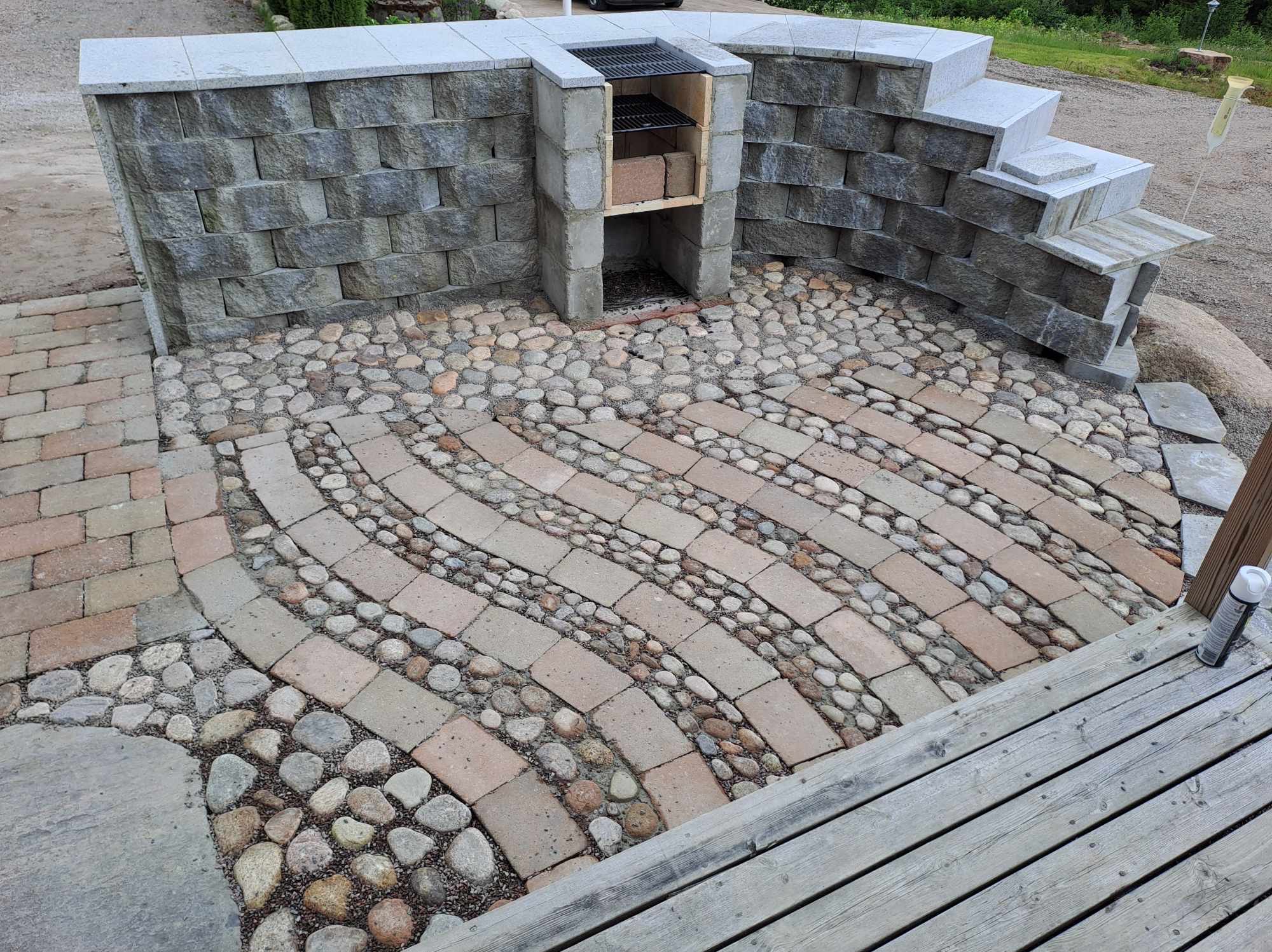Ogród z murowanym grillem, schodami i ścieżką z kostki oraz kamieni rzecznych, widok z góry.