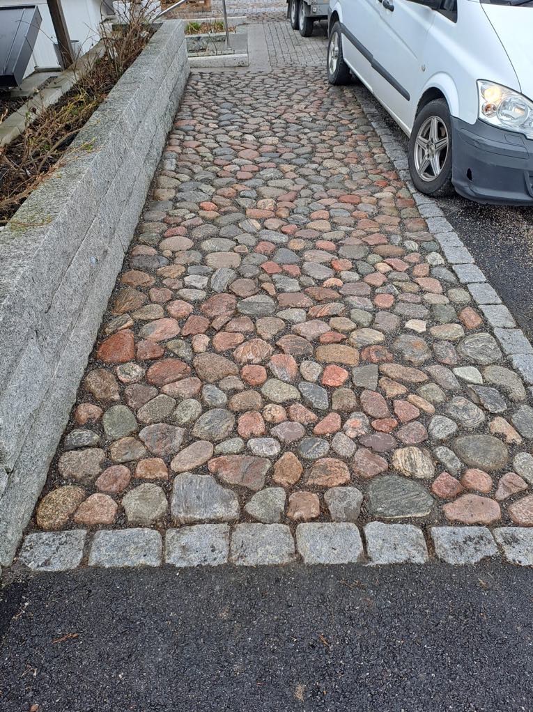 Ułożona ścieżka z nieregularnych kamieni polnych w odcieniach szarości i czerwieni, obramowana kostką granitową, z zaparkowanym białym vanem w tle.