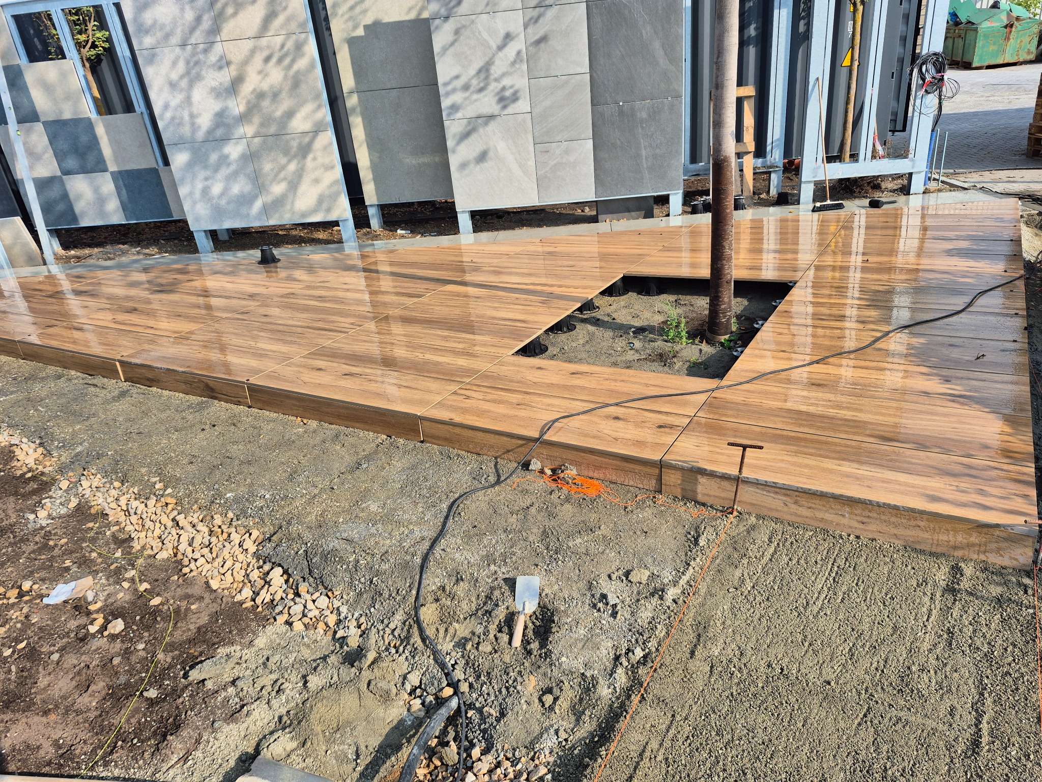 Drewnopodobna nawierzchnia tarasu z płyt ceramicznych, ułożona wokół drzewa, z widocznymi elementami montażowymi i przygotowanym podłożem.