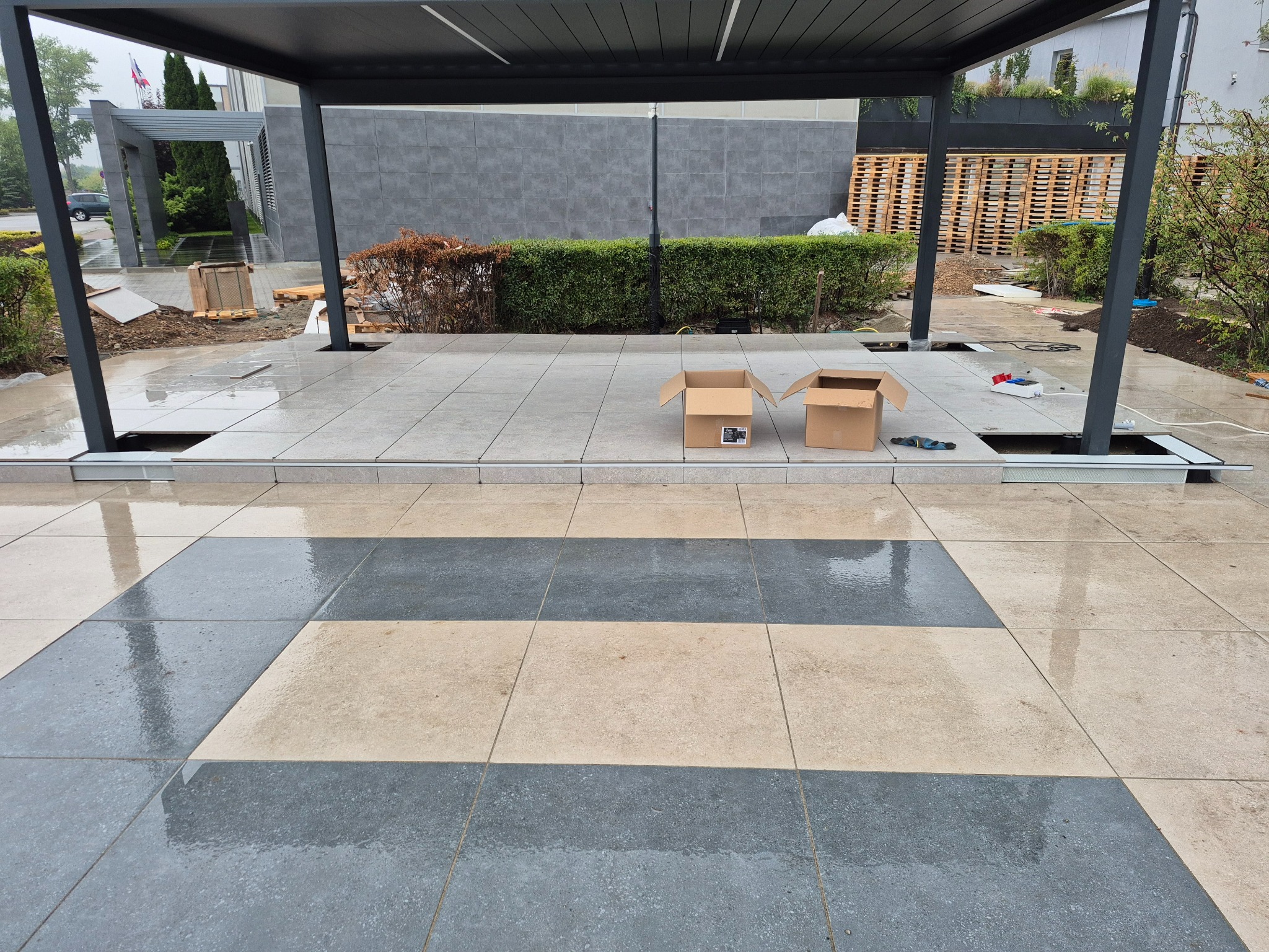 Montaż płyt tarasowych pod zadaszeniem. Dwu kolorowa kompozycja na mokrej nawierzchni. Częściowo ułożony taras z otworami na słupy konstrukcyjne.