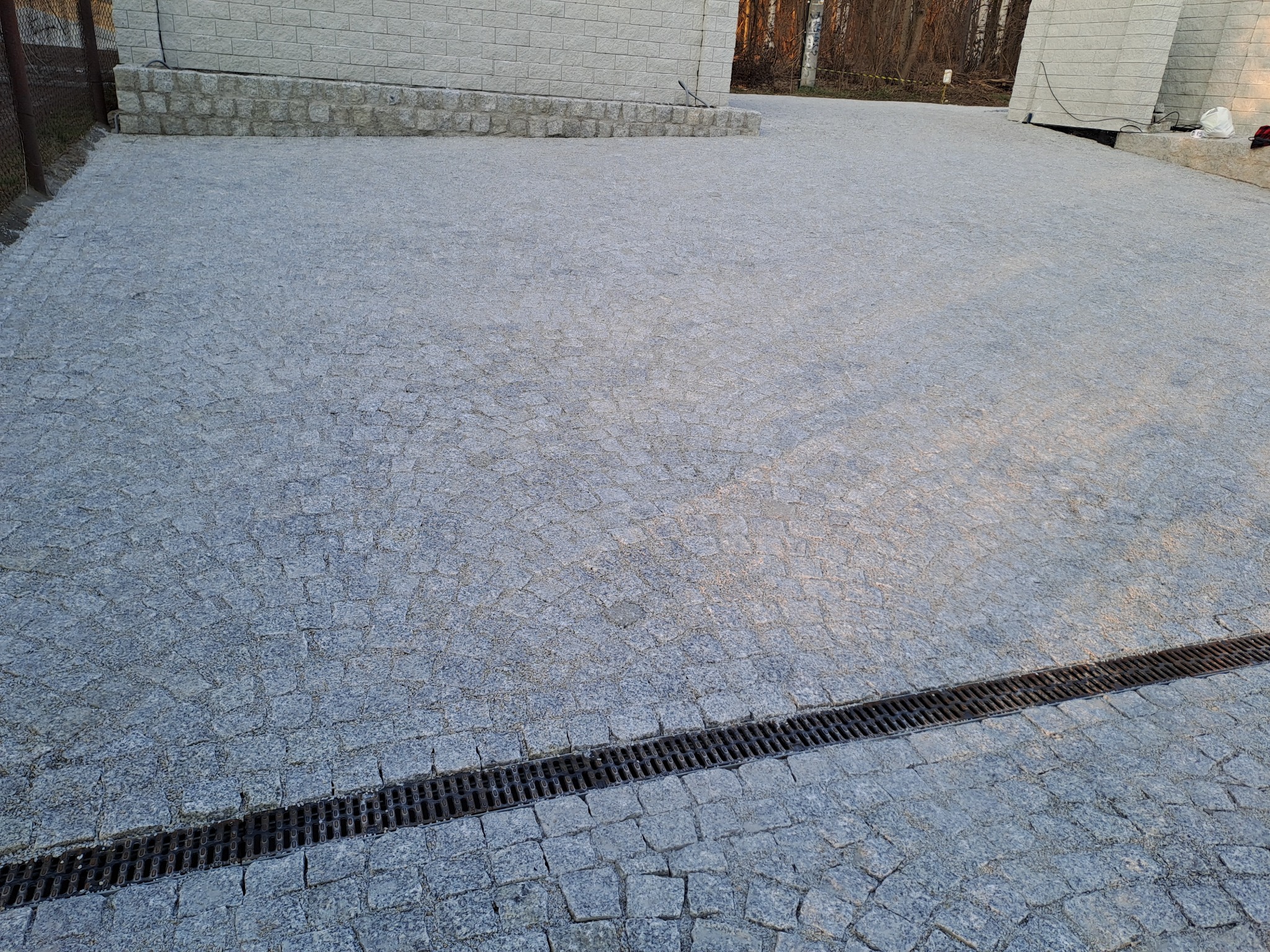 Ułożona szara kostka granitowa na podjeździe z odpływem liniowym. Widok z góry prezentuje regularny wzór i solidne wykonanie.