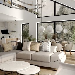 Monika Koziorowska - Jasne, przestronne wnętrze domu z otwartą kuchnią, salonem i jadalnią, z dużymi oknami, nowoczesnym oświetleniem i minimalistycznym wystrojem w odcieniach bieli i szarości.