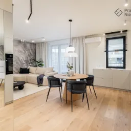 Jasne mieszkanie po home stagingu: okrągły stół z szarymi krzesłami, beżowa sofa z czarnymi poduszkami, ściana z efektem marmuru, lustrzana szafa w przedpokoju.