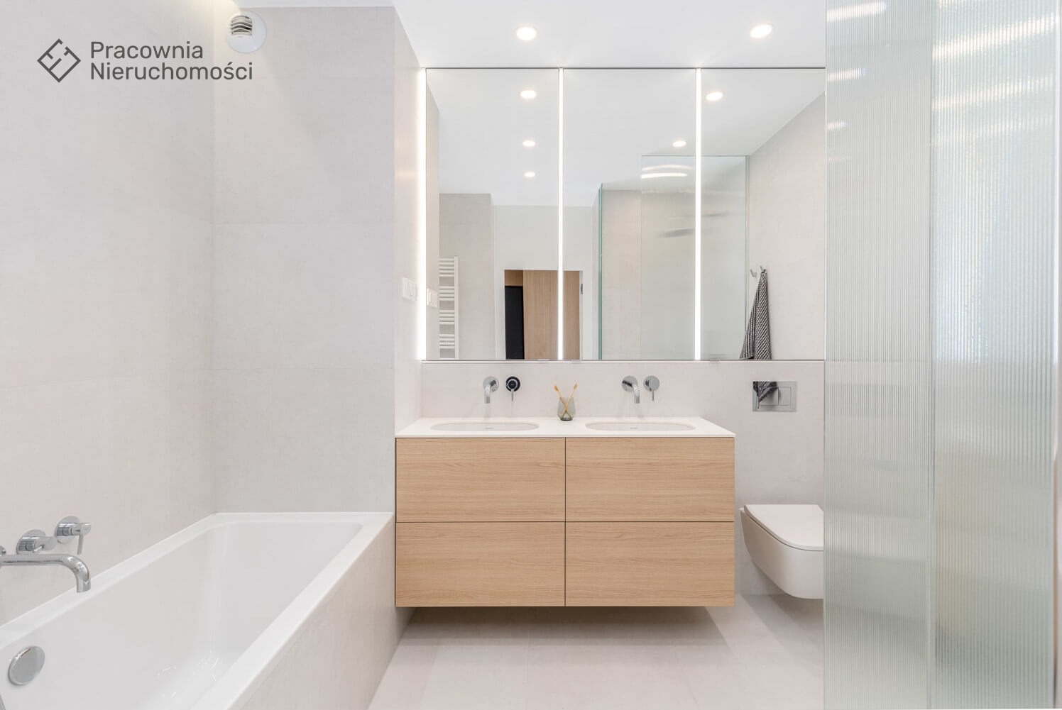 Nowoczesna łazienka w jasnych barwach z drewnianą szafką pod umywalką, podświetlanym lustrem i kabiną prysznicową z ryflowanego szkła.