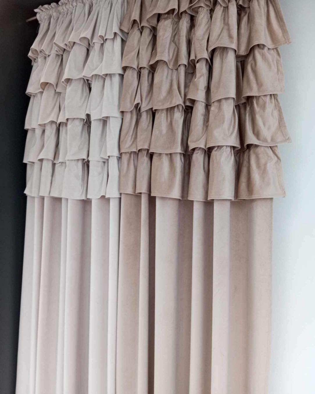 Drapowane, beżowe zasłony z falbanami, różniące się odcieniem po lewej i prawej stronie, wiszące na karniszu.