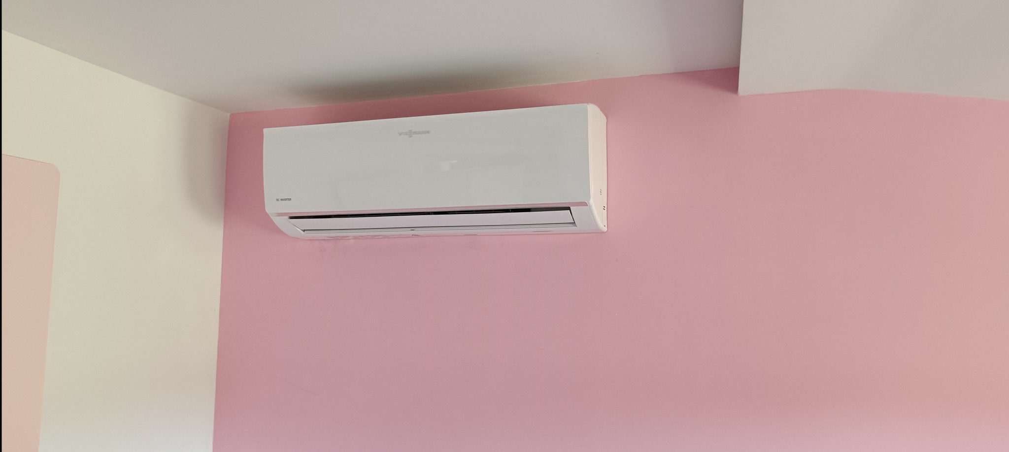 Biała jednostka klimatyzacyjna marki Viessmann zamontowana na różowej ścianie w rogu pomieszczenia.