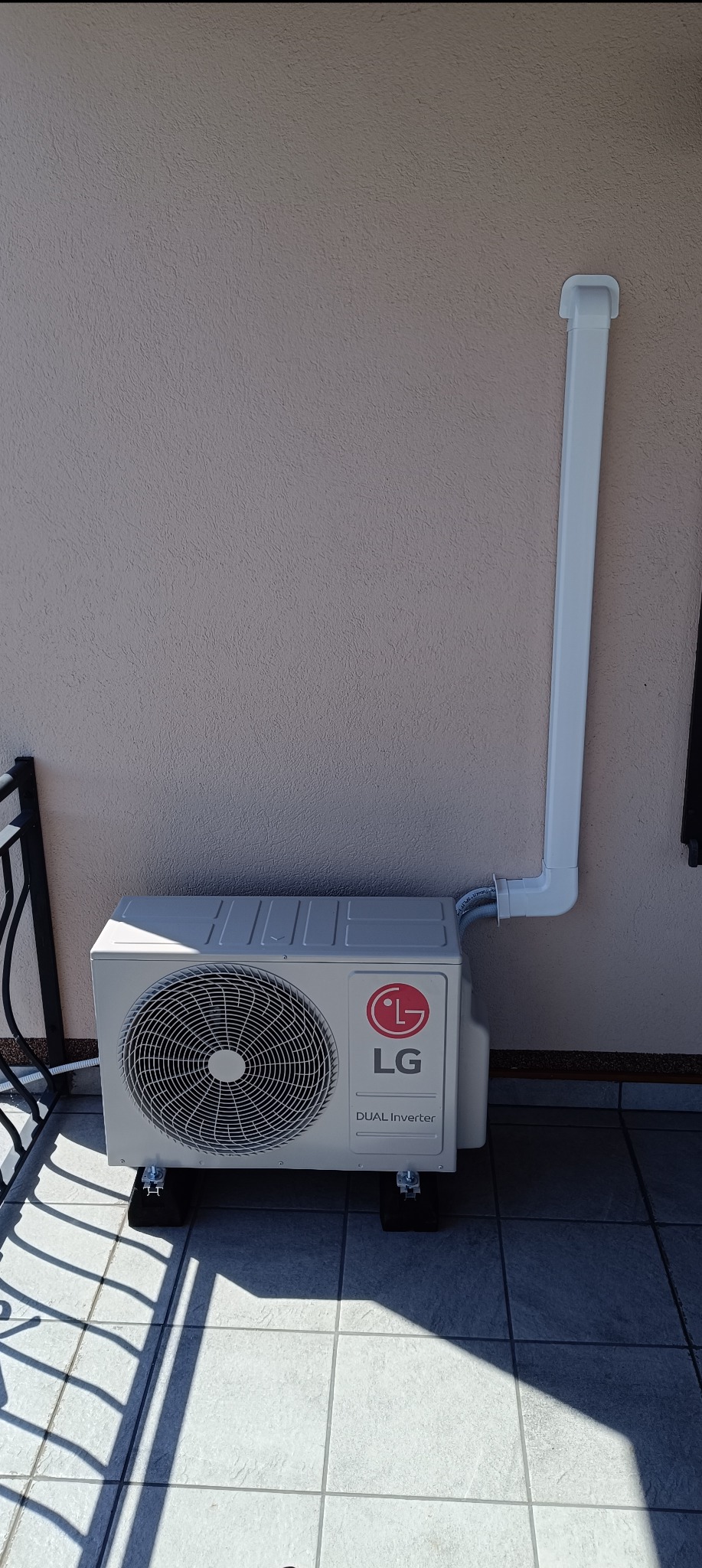 Zewnętrzna jednostka klimatyzacji LG Dual Inverter zamontowana na balkonie, z widoczną rurą odprowadzającą skropliny poprowadzoną wzdłuż ściany.
