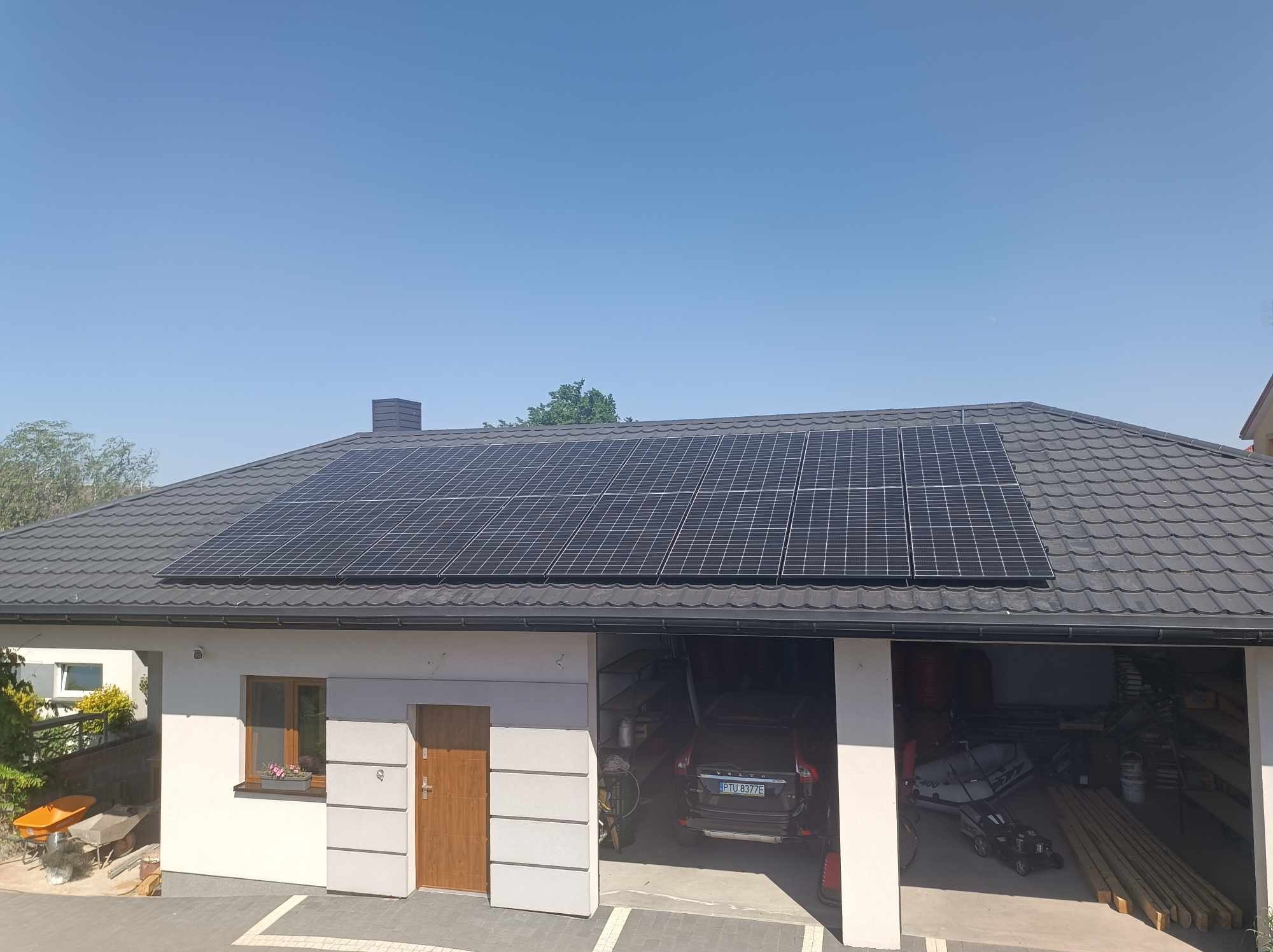 Panele fotowoltaiczne na dachu domu jednorodzinnego z garażem, widok z góry, błękitne niebo w tle.